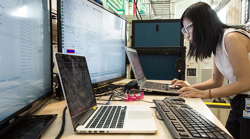 Photo of NREL researcher Fei Ding wearing protective eyewear while working on a computer in a laboratory.