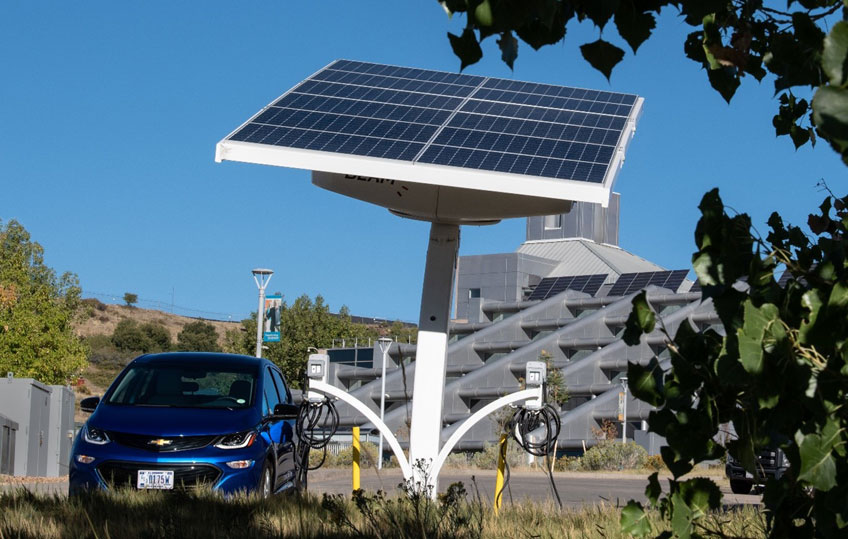 An electric vehicle charges at a port with an integrated solar panel in front of an NREL building.