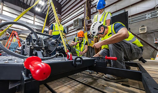 Four people in hard hats and safety vests work on a large metal piece of equipment