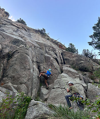 Cory Frontin climbing a rock face while Calum Kenny belays