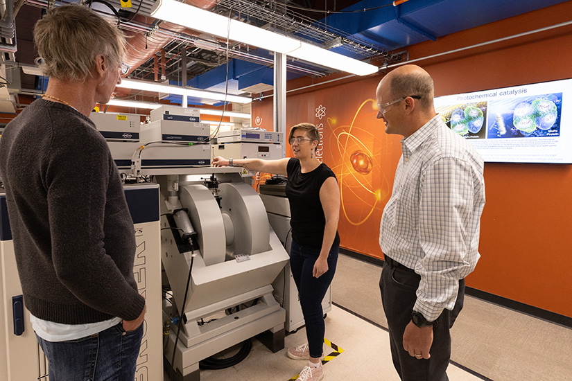 A group of researchers talking and standing next to a machine. 
