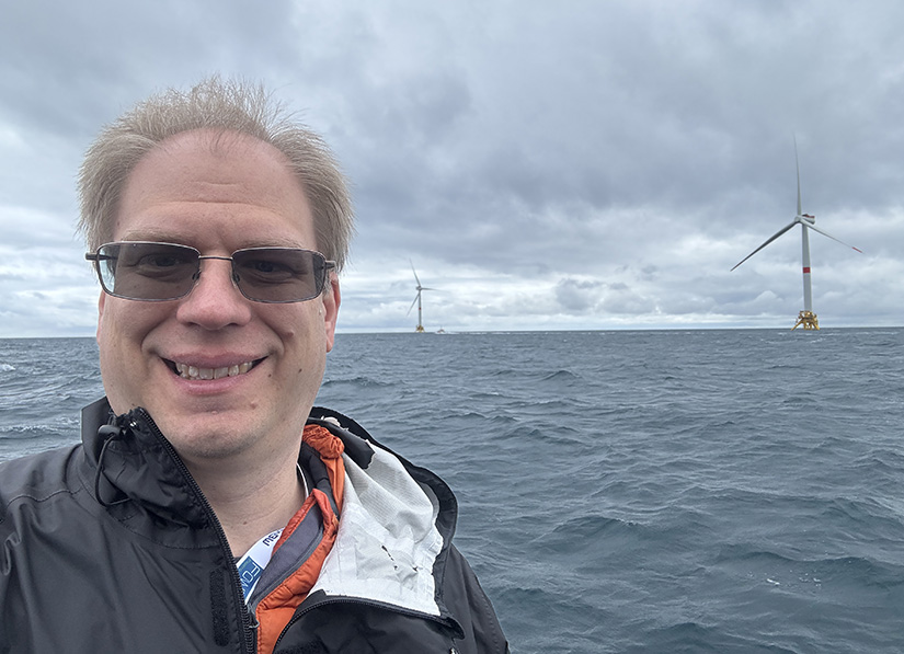 A man with wind turbines in the background at sea.