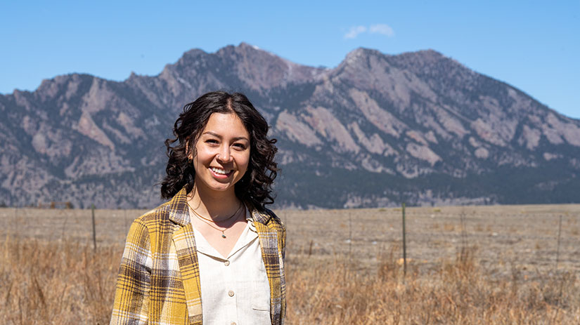 Tina Ortega stands in a grassy field with mountains in the background