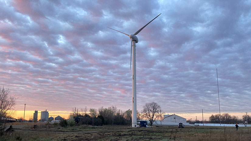 A small wind turbine next to a farm at dawn