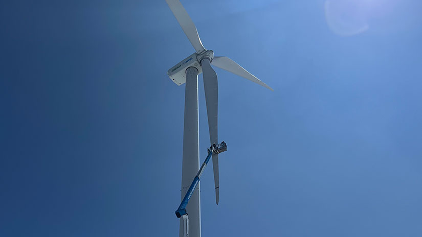 A technician in an extended aerial lift works on the blade of a wind turbine