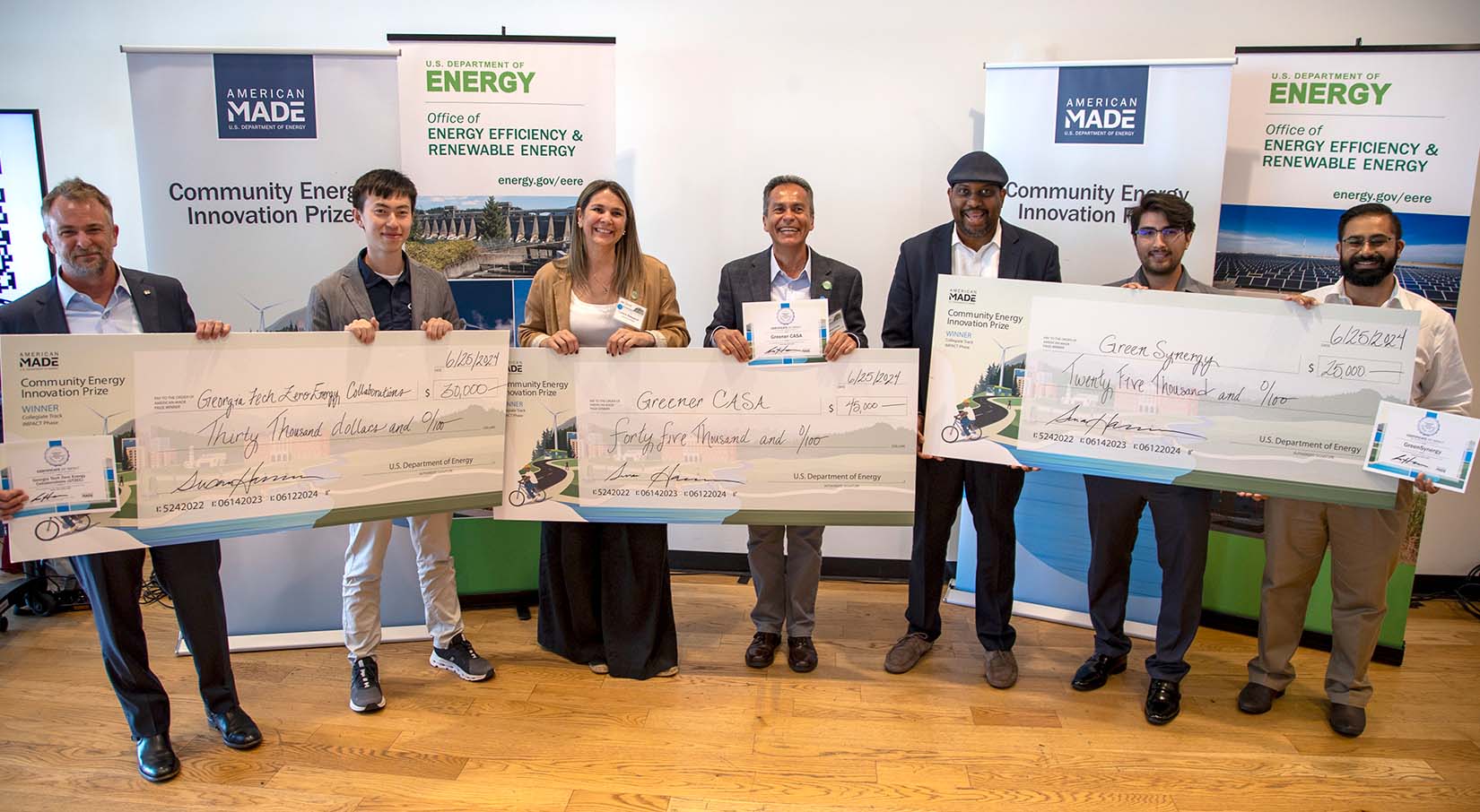 Seven people holding large checks and certificates.