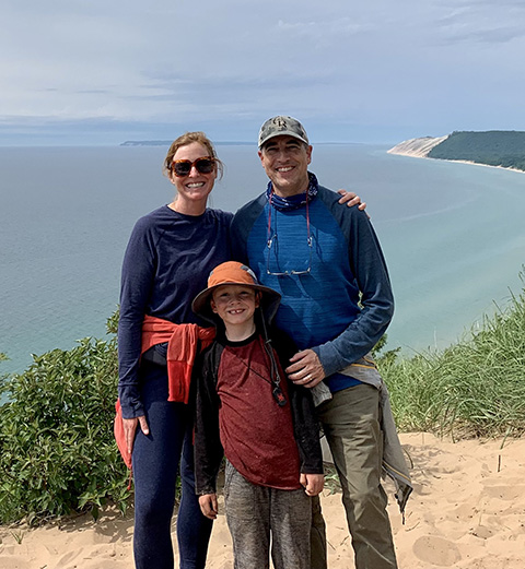 Two adults and a child stand on an overlook above a body of water.