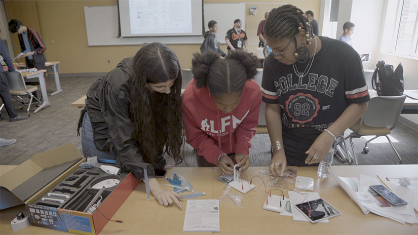 Group of students work over technology at a table