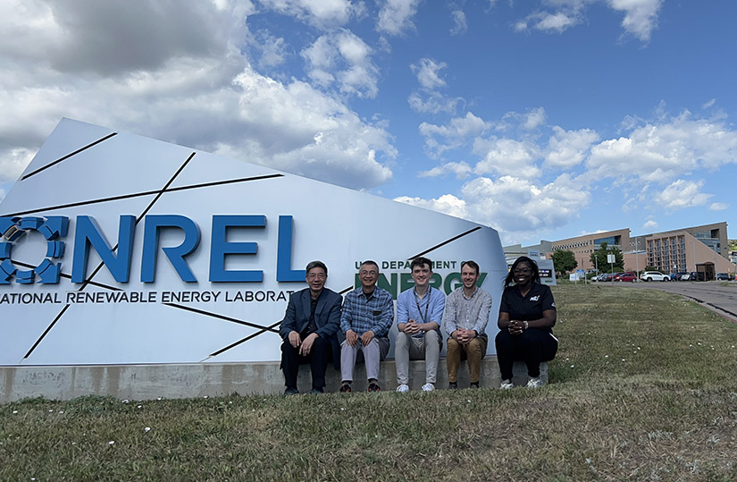 Five people sit in front of a sign that reads: NREL National Renewable Energy Laboratory. 