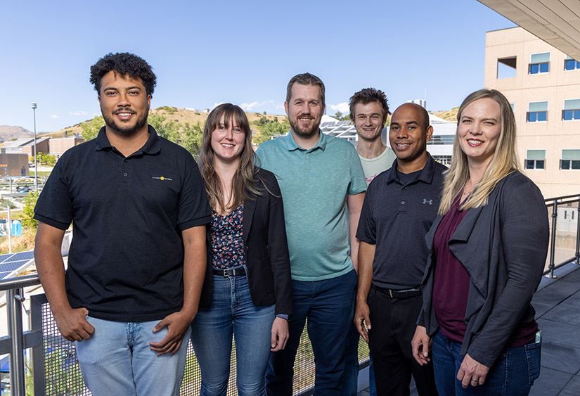 Six people smile for the camera, posed on an outdoor balcony. 