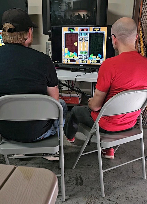 Two people sitting in chairs facing a screen with a video game on it. 