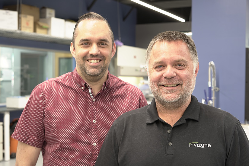   Two men pose for a photo inside a laboratory.