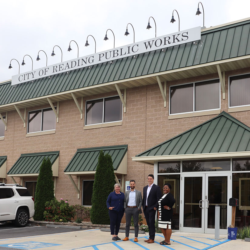 Four people stand outside in a parking lot in front of Public Works building