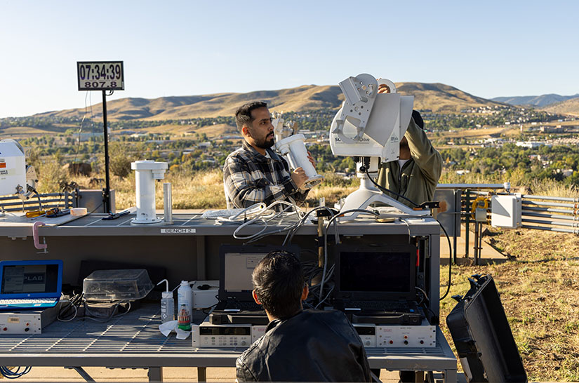 Three people setting up instrumentation on a hilltop.