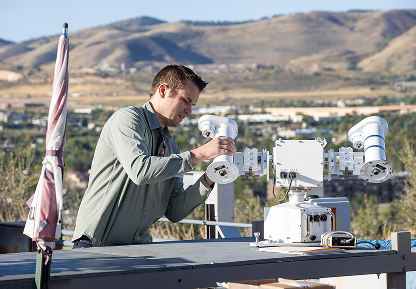 A person holding part of a solar instrument in their hand in front of a hilly background.