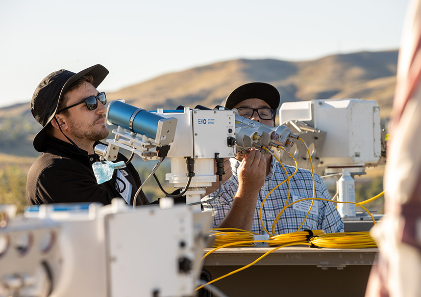 Two people wearing hats and sunglasses looking into solar instrumentation. 