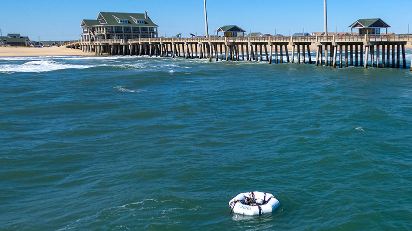 A raft with equipment on top floats a short distance from a wooden pier