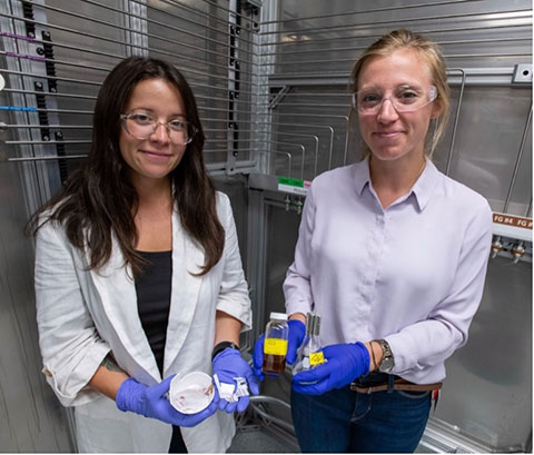 Knauer and another person wearing safety goggles and gloves and holding lab supplies