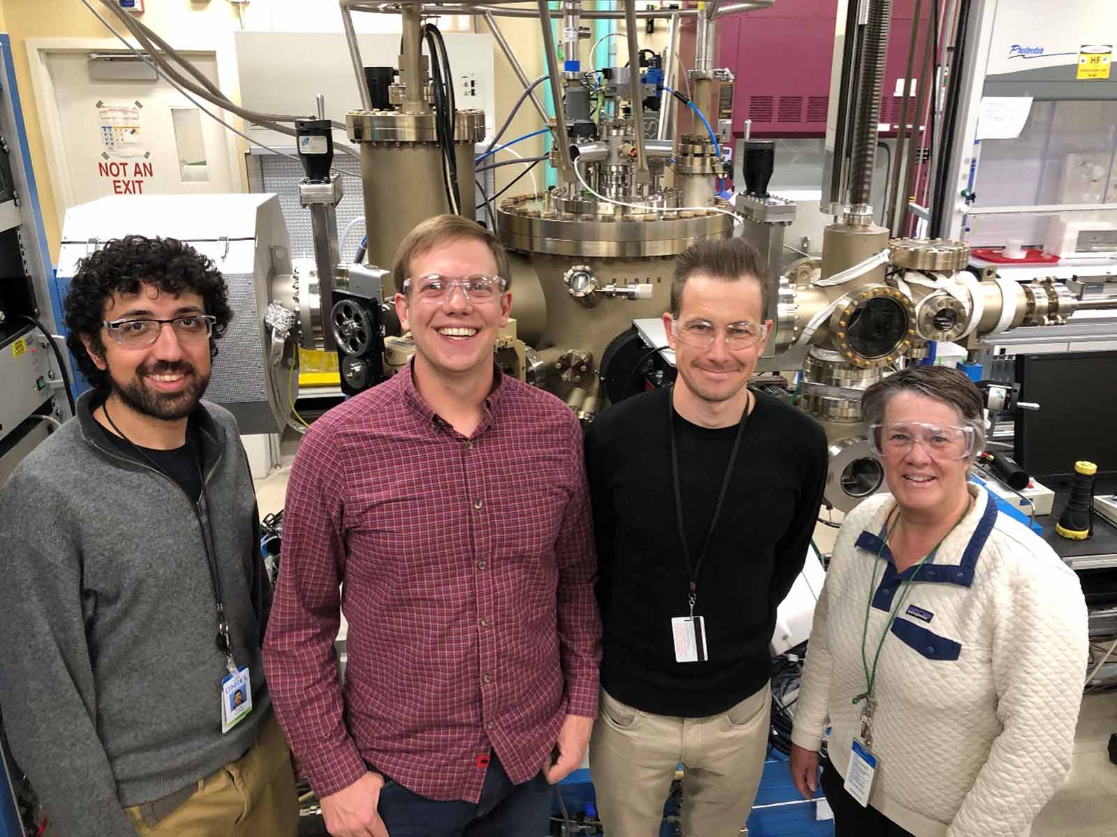 Four people side-by-side in front of laboratory machines.