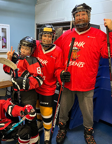 Suzanne MacDonald, her son, and her husband wearing hockey gear and brandishing hockey sticks