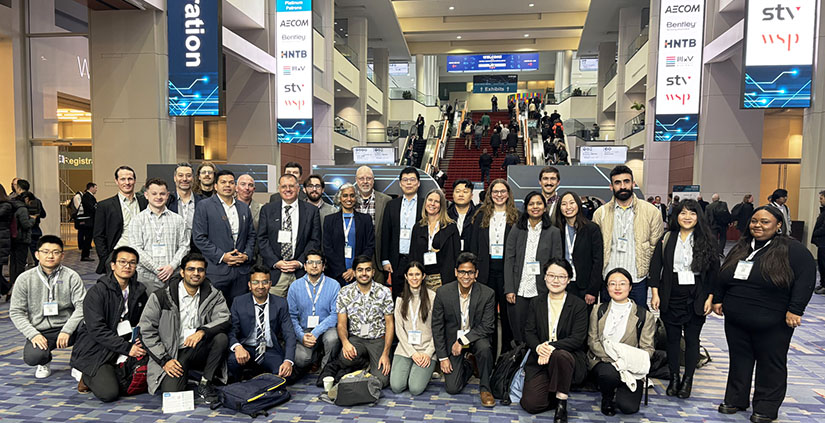 19 people posing for a photo in the lobby of a large hall.