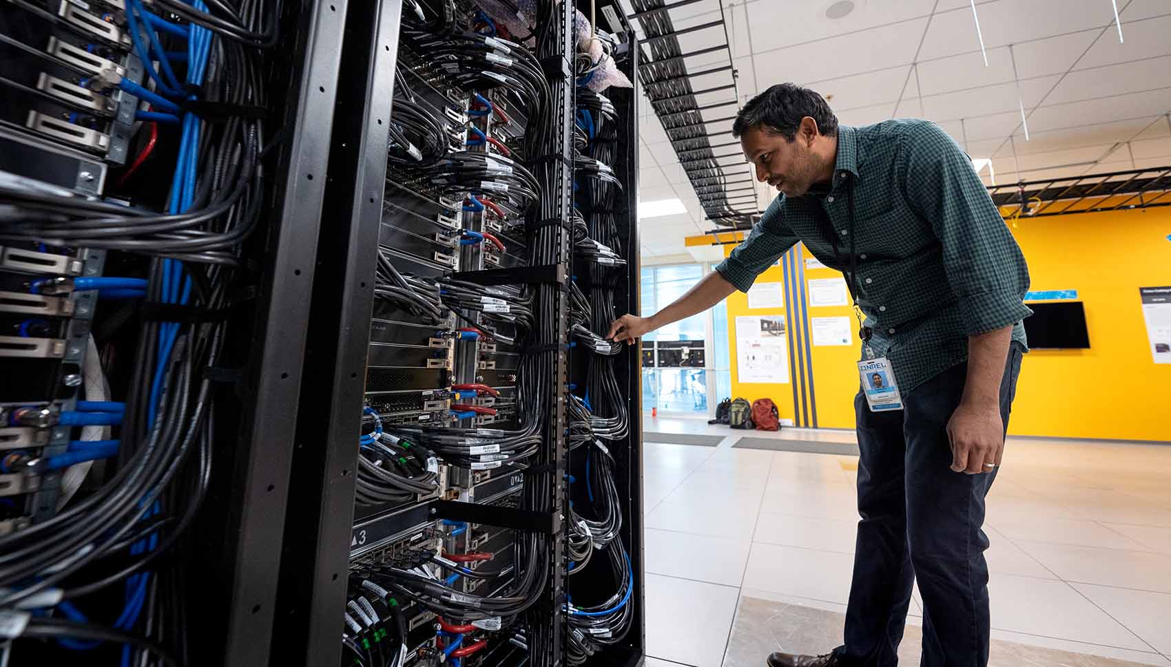 A man inspects cables connected to a large server rack.