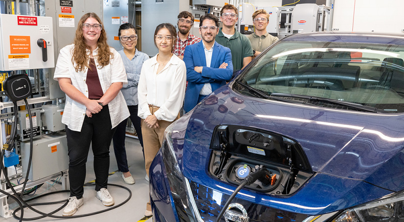 A group of seven people stand next to an electric vehicle in a laboratory setting.