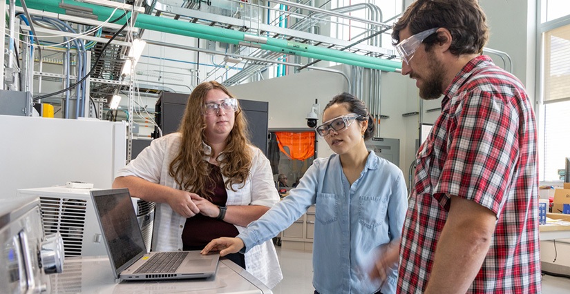 Three people stand in a laboratory around a laptop.