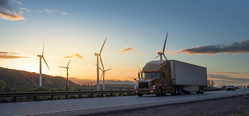 A semi truck driving in front of wind turbines.