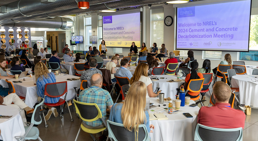 A conference room of people sit at round tables to watch a presentation.