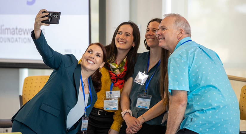 Four people in business casual attire pose for a cellphone selfie.