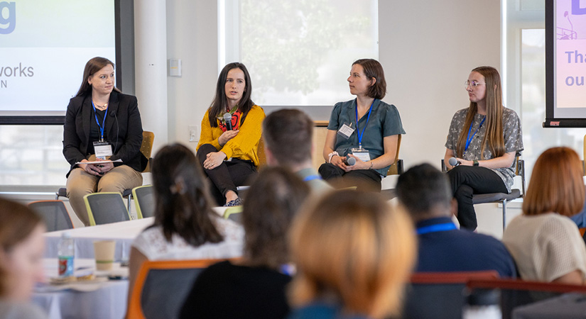 Four people sit in the front of a conference room.