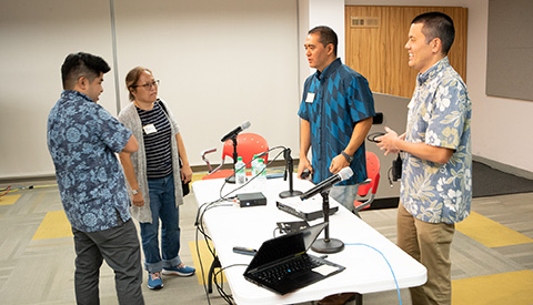 Four people standing at a table with microphones.