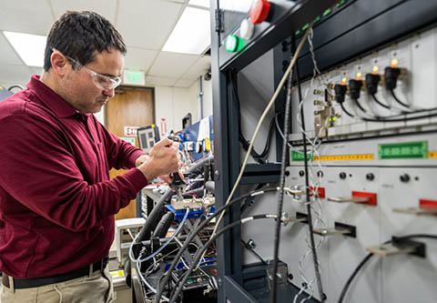 Gilbert Moreno works with a piece of power electronics thermal management equipment in a laboratory.