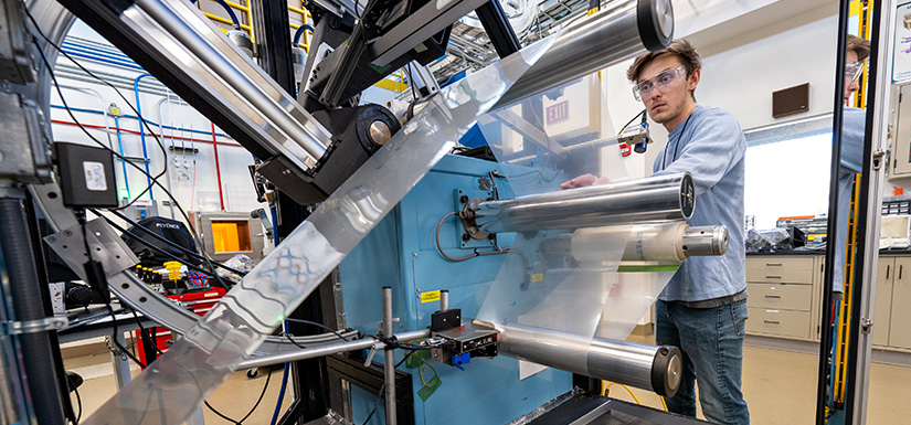 A researcher with safety glasses in a laboratory operates a roll-to-roll web line machine, which rolls films for hydrogen fuel cells.