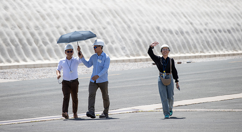 Three people smiling and waving while walking outside.