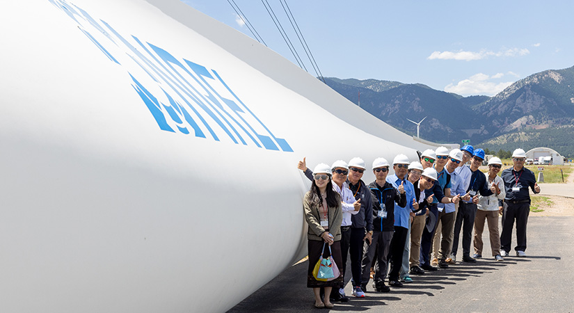 A large group of people standing outside infront of a wind turbine blade.