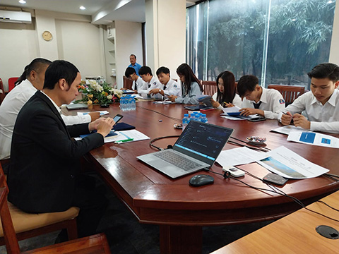 A group of individuals sit around a large wooden conference table. There is an open laptop in the corner of the table.