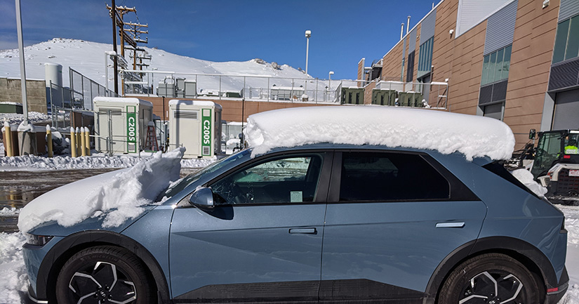 An electric vehicle is parked outside an NREL laboratory with snow accumulated on top of it.