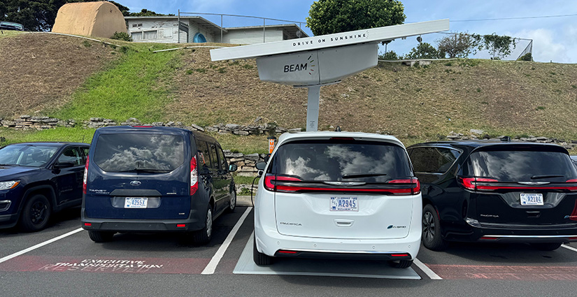 An electric vehicle plugged into a charger powered by a solar array mounted above the charging spot.