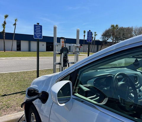 : A white electric vehicle in a parking spot plugged into an EV charger.