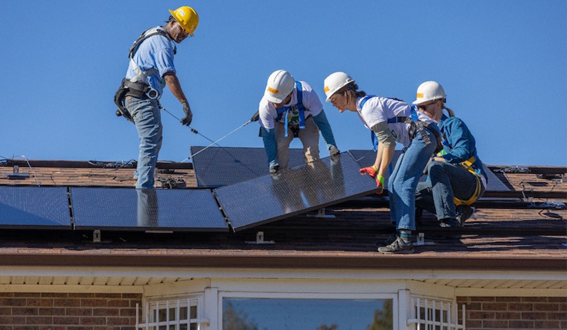 Four people install solar panels on the roof of a house.