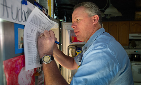 A man writing on a piece of paper while holding it against the wall.