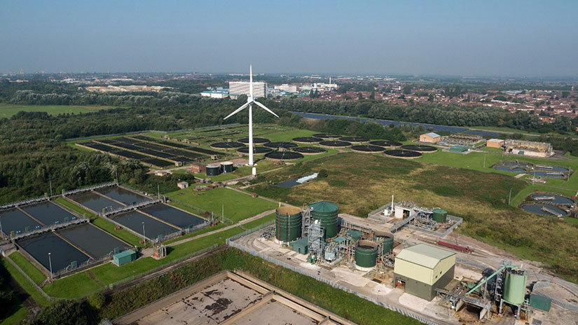 Wind turbine stands in the middle of a field next to solar panels and hydro power plant