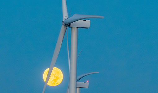 Wind turbine in the sky with the moon behind it