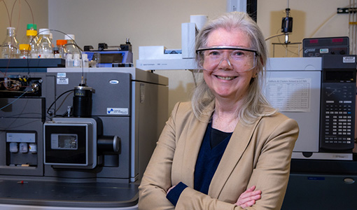 Portrait of Maureen McCann with arms crossed wearing safety goggles in a lab.