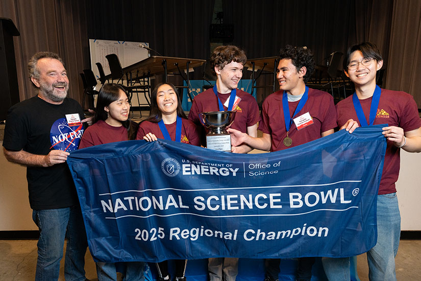 A teacher and five teens hold up a flag that reads: National Science Bowl 2025 Regional Champion.