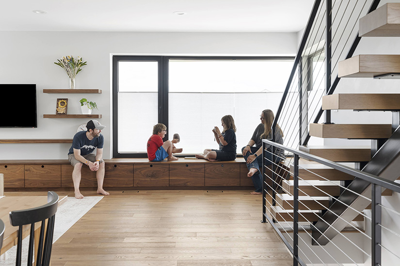 Two parents and two children sit on a bench under a window in a newly built home.