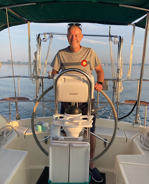 A person smiles while steering a sailboat.