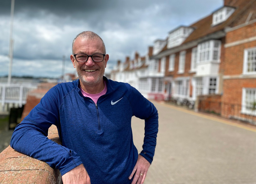 A person leans against a brick wall with quaint houses in the background.